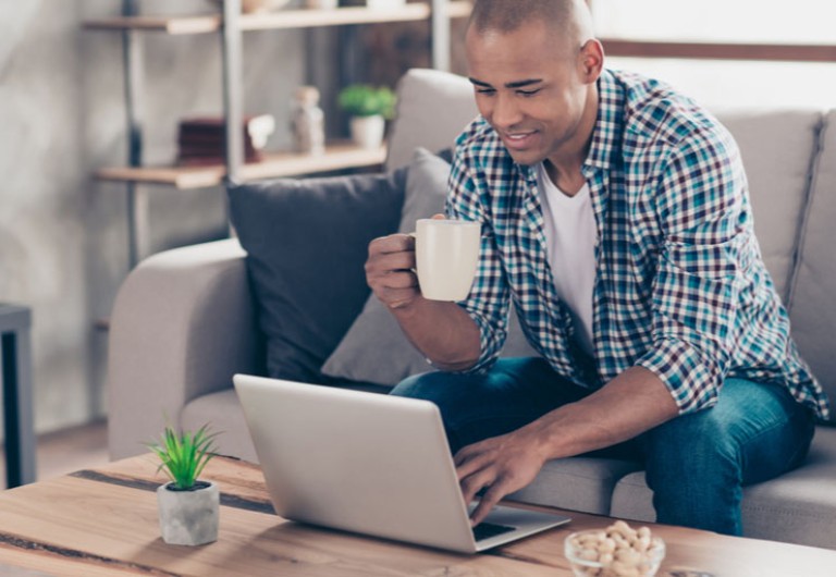 Man holding a cup of coffee while checking his laptop