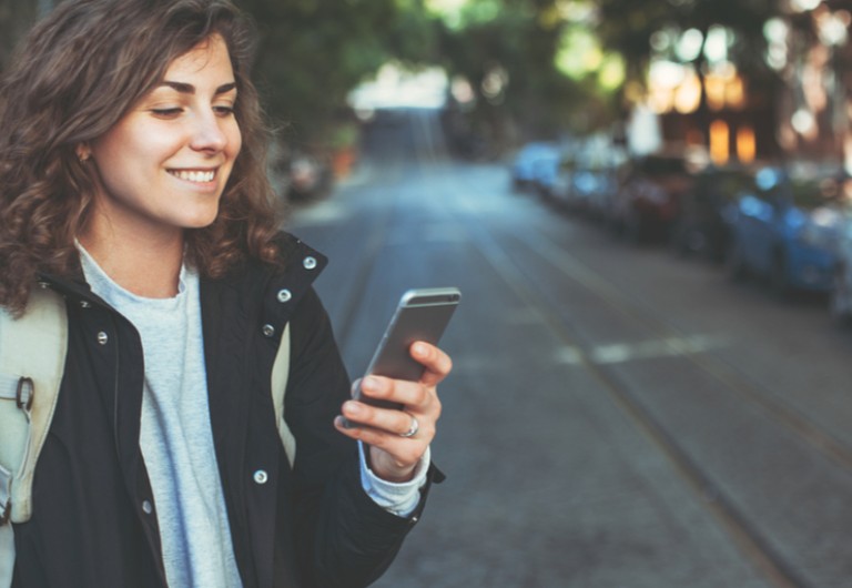 Woman on a street looking at her mobile phone and smiling