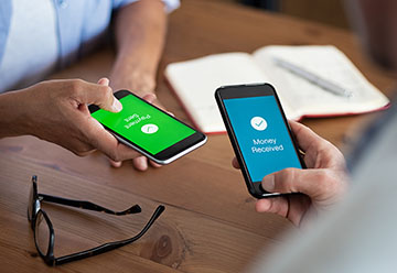 Two mobile phones, one sending and the other receiving an online money transfer