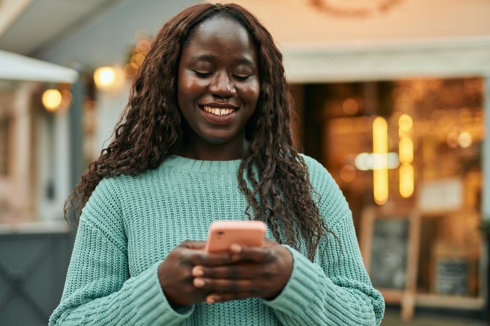 Woman standing outside smiling and looking at her mobile phone