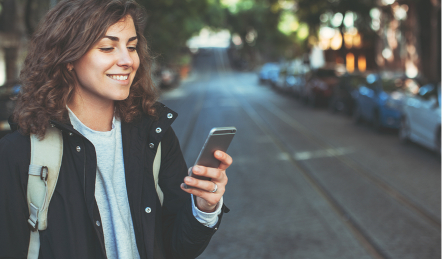 Woman on a street looking at her mobile phone and smiling