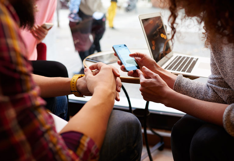 Man and woman sitting at a table by a cafe window with a laptop on the table and the woman holding a smartphone